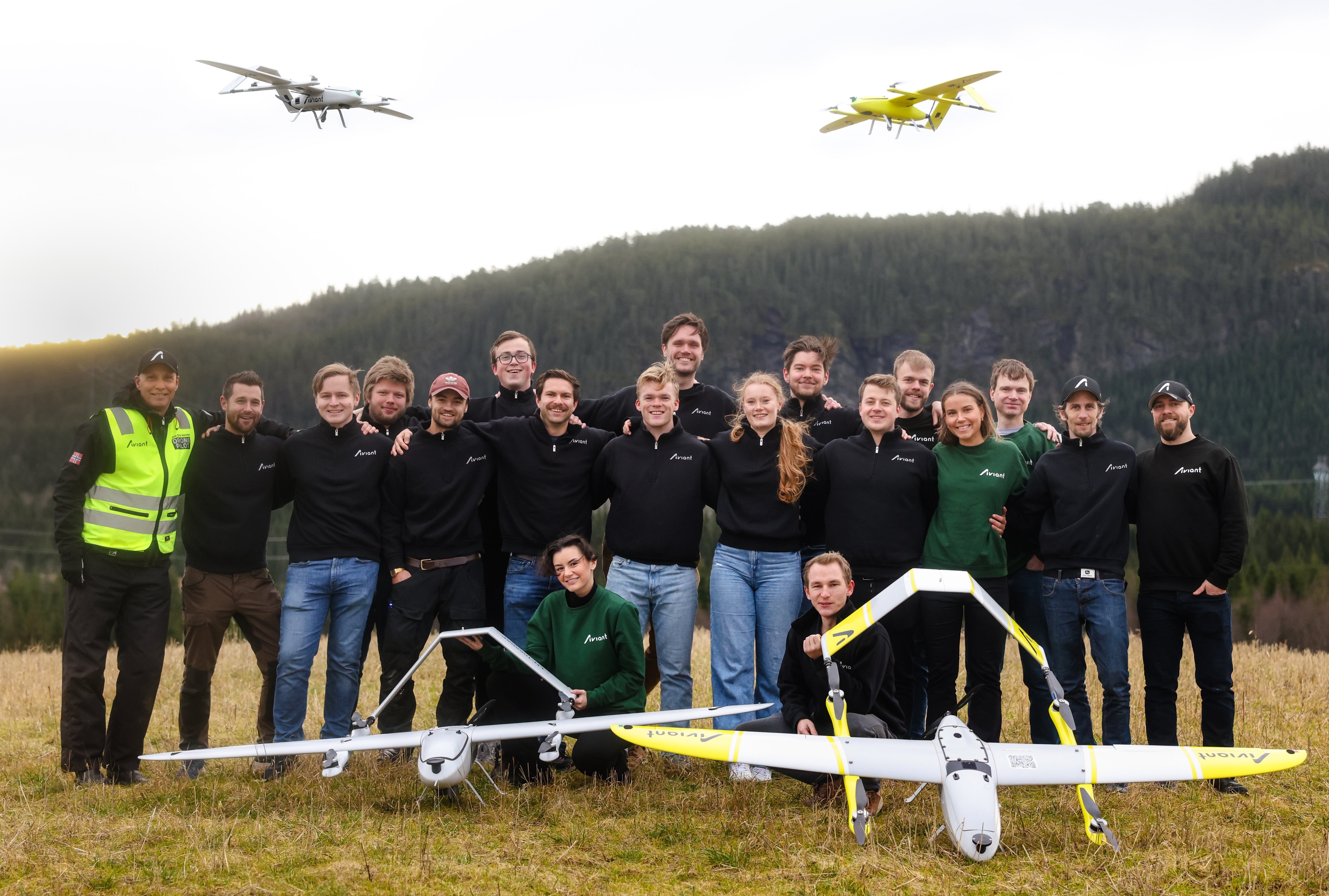 An image of the whole Aviant team posing with two drones flying in the air above them